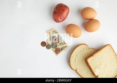 Uno studio girato su bianco guardando giù su alimenti di base uova, pane e patate con valuta che rappresenta l'economia Foto Stock