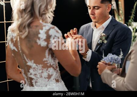 Lo sposo concentrato mettendo l'anello di nozze sul dito della sposa dopo che hanno detto sì l'uno all'altro. Appena sposato Foto Stock