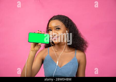 bella giovane donna africana che mostra il suo schermo del telefono, indossando le cuffie Foto Stock