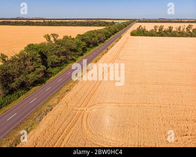 Veduta aerea di una stretta strada di campagna asfaltata grigia, che attraversa un paesaggio con campi e prati. Foto Stock