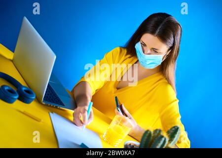 donna in una blusa gialla lavora a distanza a casa durante una pandemia Foto Stock