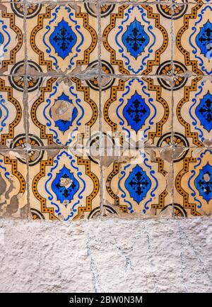 Piastrelle gialle e blu su una parete grigia con crepe nel motivo Foto Stock