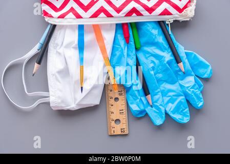 Ritorno a scuola durante la pandemia del coronavirus COVID-19. Custodia a matita per bambini piena di materiale scolastico, guanti e maschera facciale. Foto Stock