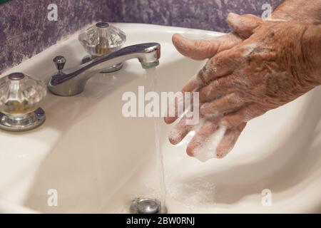 Uomo lavando mani saponate nel lavello del bagno con acqua che scorre giù lo scarico Foto Stock