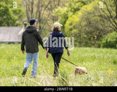 Berks County, Pennsylvania - 5 maggio 2020: La coppia più anziana prende il cane per una passeggiata nel parco il pomeriggio di primavera. Foto Stock