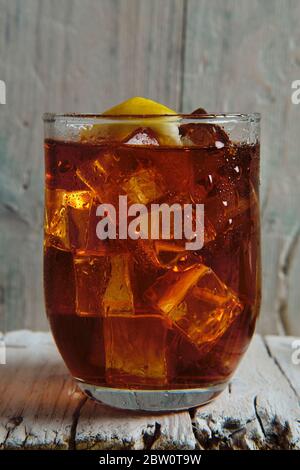 primo piano di un bicchiere pieno di cola con ghiaccio e. limone su base di legno Foto Stock