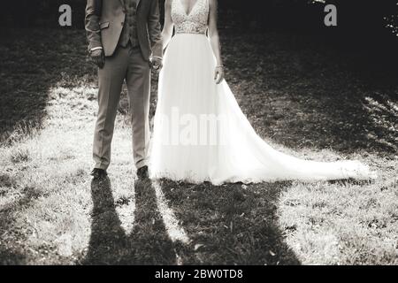 Foto in bianco e nero di una coppia di nozze in piedi sull'erba nel parco. Vista in retroilluminazione con ombre rivolte verso la fotocamera. Concetto di giorno di nozze. Foto Stock