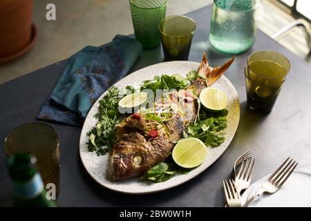 Piatto di pesce intero arrosto in un tavolo con bicchieri e tovagliolo Foto Stock