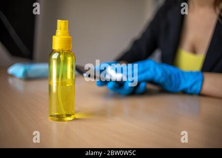 Mano da donna in guanti blu igienizzante pulizia smartphone cellulare su superficie del tavolo in legno con salviette bagnate e alcol Foto Stock