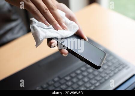 Lavorare da casa, pulire e disinfettare smartphone e computer portatile con salviette umide Foto Stock