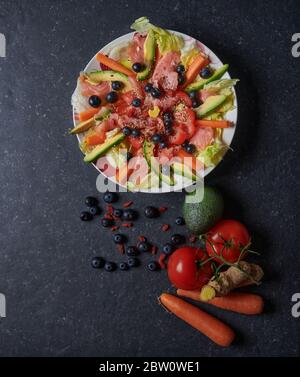Insalata di salmone con salmone affumicato, verdure fresche, mirtilli e semi, avocado, carote, insalata di ghiaccio, pomodori, zenzero, semi di sesamo, semi di lino A. Foto Stock