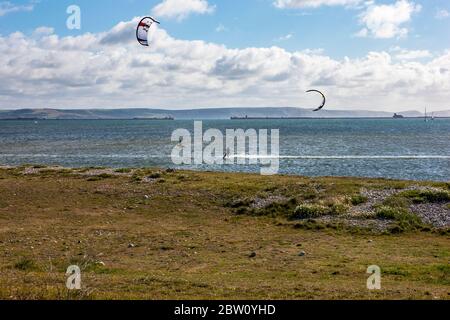 I windsurfisti praticano una bella mattina soleggiata sulle acque della baia di Weymouth contro un cielo blu nuvoloso Foto Stock