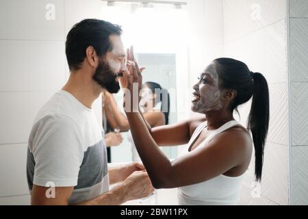 Donna che applica maschera di bellezza e detergente per la pelle all'uomo Foto Stock