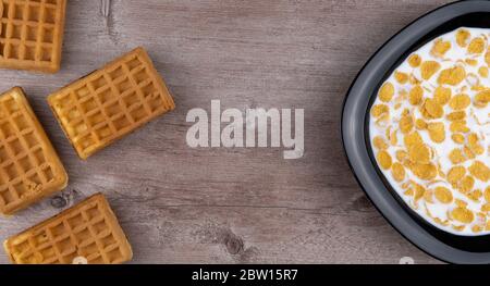 piatto con cornflakes nel latte e waffle su sfondo di legno. vista dall'alto, spazio per fotocopie. Foto Stock