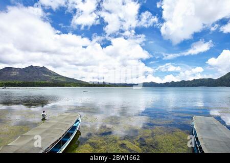 Il lago Batur è molto ampio con un cielo nuvoloso drammatico, sembra che un pescatore stia cercando pesce al centro di esso Foto Stock