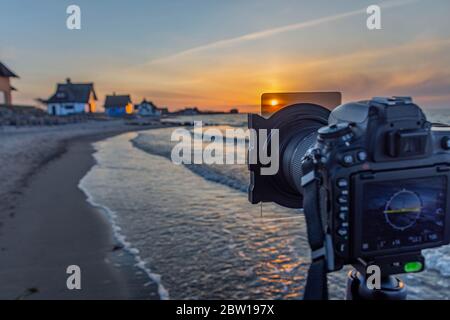 Fotocamera DSLR sul treppiede con filtro ND da fotografare al tramonto sul Mar Baltico, scattando una foto di un bellissimo tramonto, utilizzando un filtro grigio al tramonto, s Foto Stock