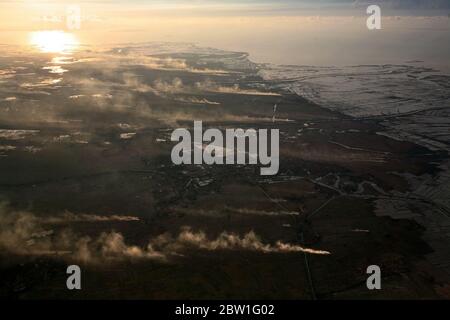 Vista aerea del paesaggio costiero che mostra campi agricoli, fumo, canali, allevamenti di gamberi marini e stagni di evaporazione del sale in Tangerang regency, provincia di Banten, Indonesia, sono visti attraverso una finestra di un aereo che si avvicina all'Aeroporto Internazionale Soekarno Hatta di Giacarta. Foto Stock