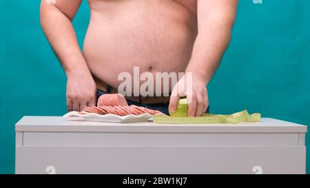 l'uomo con una pancia grassa sceglie tra salsiccia e mela verde. Il concetto di dieta e di volontà. Foto Stock