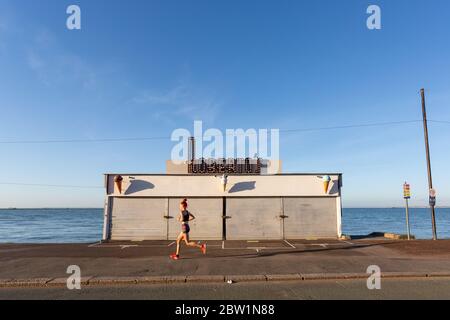 Southend-on-Sea, Regno Unito. 29 maggio 2020. Un jogger di mattina presto passa davanti ad un cafe chiuso sul lungomare. Cielo limpido e partenza calda al Venerdì mattina a Southend-on-Sea-Sea. Penelope Barritt/Alamy Live News Foto Stock