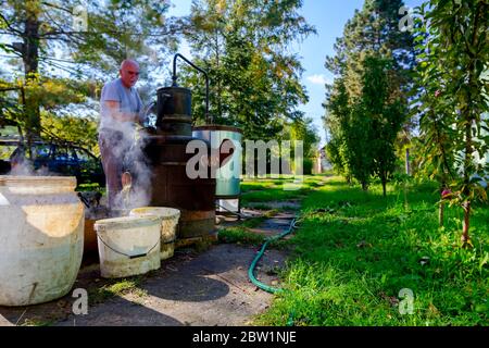 L'uomo sta scaricando la caldaia di distilleria fatta in casa di rame per rilasciare vinacce di frutta usate, facendo scnapps di luna-lustro, bevande alcoliche come marca Foto Stock