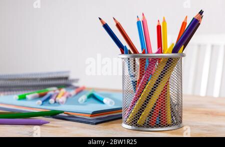 Primo piano di matite e pastello a cera con carte e libri da lavoro sulla scrivania in interni leggeri. Concetto di educazione artistica e d'arte Foto Stock