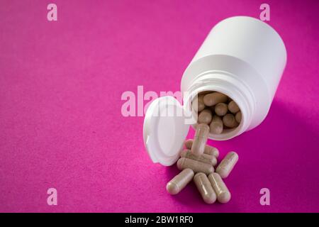 Pillole mediche versate da bottiglia di pillola bianca su sfondo rosa Foto Stock