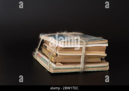 Mezza dozzina di libri vecchi accatastati e legati con una corda sfilacciata su uno sfondo nero. Concetto retrò. Ancora vita di libri. Foto Stock