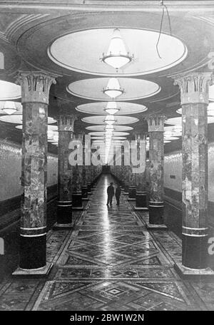 Marmo e mosaico decorano la nuova e sontuosa stazione della metropolitana di Mosca. Decorata sontuosamente e con l'aspetto di un hotel di lusso, è stata completata una nuova stazione della metropolitana di Mosca. Colonne di marmo sostengono il tetto e il pavimento è intarsiato di mosaico, mentre grandi pendenti inondano la piattaforma di una luce soffusa diffusa attraverso il vetro smerigliato. La nuova stazione è la Kievskaya, che prende il nome da L. M. Kaganovich, Commissaria popolare per le ferrovie, e corre da Piazza Smolensk alla piazza della stazione ferroviaria di Kiev. Spettacoli fotografici: La piattaforma splendidamente rifinita della stazione di Kievskaya o Foto Stock