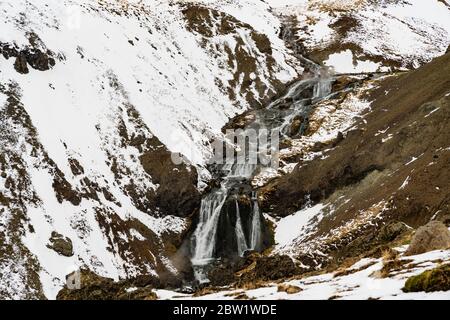 Una piccola cascata che scorre attraverso la neve e le rocce Foto Stock