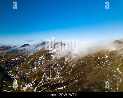 Drone foto della cima di una catena di montagna coperta nelle nuvole e illuminato dal sole del mattino Foto Stock