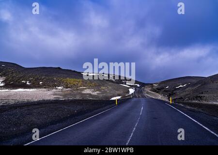 Una strada solitaria alta su una catena montuosa che si starrona fuori dal panorama, circondata da aridi paesaggi montani Foto Stock