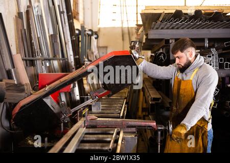 Lavorazione di tubi quadrati con bearded focalizzata su macchine per sega a nastro industriali in officina per la lavorazione dei metalli Foto Stock