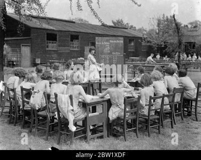 Gli studenti all'aperto possono sfruttare al massimo l'ondata di caldo. Il minimo di vestirsi e il massimo dell'aria fresca e del figlio è la regola alla Bow Road Open-Air Day School nel East End di Londra, dove gli alunni si stanno revellendo nell'onda di calore. Foto: Gli alunni leggermente rivestiti alla lezione nella scuola all'aperto di Bow Road. 26 maggio 1937 Foto Stock