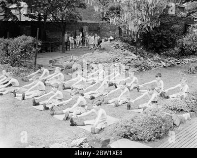 Gli studenti all'aperto possono sfruttare al massimo l'ondata di caldo. Il minimo di vestirsi e il massimo dell'aria fresca e del figlio è la regola alla Bow Road Open-Air Day School nel East End di Londra, dove gli alunni si stanno revellendo nell'onda di calore. Foto: Esercizio fisico per gli alunni con la leggera clade della scuola all'aperto di Bow Road. 26 maggio 1937 Foto Stock