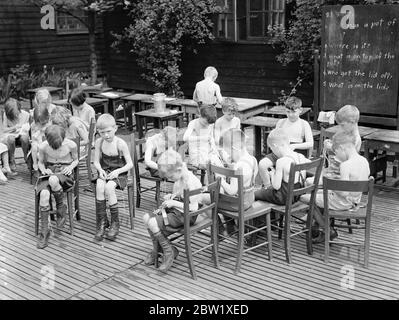 Gli studenti all'aperto possono sfruttare al massimo l'ondata di caldo. Il minimo di vestirsi e il massimo dell'aria fresca e del figlio è la regola alla Bow Road Open-Air Day School nel East End di Londra, dove gli alunni si stanno revellendo nell'onda di calore. Foto: Gli alunni leggermente rivestiti alla lezione nella scuola all'aperto di Bow Road. 26 maggio 1937 Foto Stock