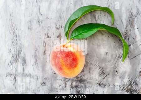 Pesca con foglia su fondo grigio di cemento. Pesca dolce fresca con snocciolata. Vista dall'alto frutta fresca di pesca biologica Foto Stock