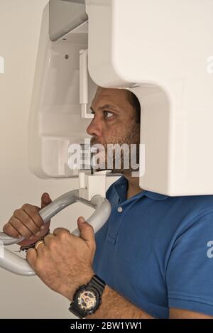 Paziente nella sala di radiografia della clinica dentale per vedere la salute dei suoi denti che mordano la gomma del dispositivo di ultima tecnologia. Foto Stock