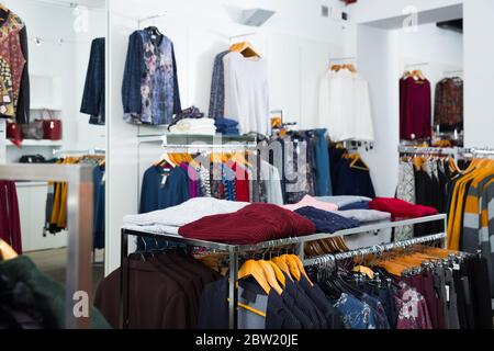 Varie camicette e cardigan su grucce e piani di appoggio in negozio di abbigliamento interno Foto Stock
