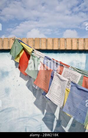 Parete blu con bandiere di preghiera tibetane come decorazione. Giornata di sole con ombre. Blu, rosso, bianco, giallo, verde. Terrazza attico decorazione. Souvenir da A. Foto Stock