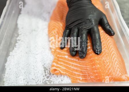 Master shusi con guanti neri igienici pulizia e la preparazione di un enorme salmone fresco.salare il pesce in una ciotola. Cucina e concetto di cibo Foto Stock