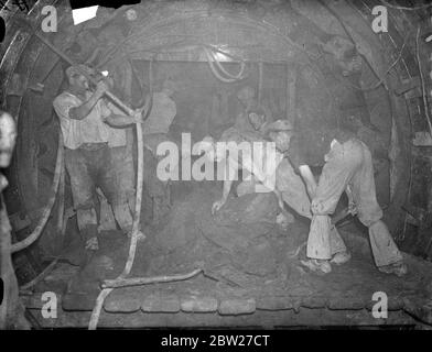 600 uomini stanno scavando un tunnel sotto le trafficate strade di North London per la nuova metropolitana di tre miglia che collegherà l'attuale capolinea della metropolitana a Highgate con la ferrovia di Londra e Nord Est alla stazione di Finchley. Si stima che il lavoro richiederà 15 mesi e che il nuovo tubo sarà terminato verso la fine del 1938. Ci sarà una sola stazione a Highgate. Lavoratori che guidano il tunnel attraverso la terra 130 piedi sotto. Gli uomini in background stanno conducendo l'attacco. 20 luglio 1937 Foto Stock