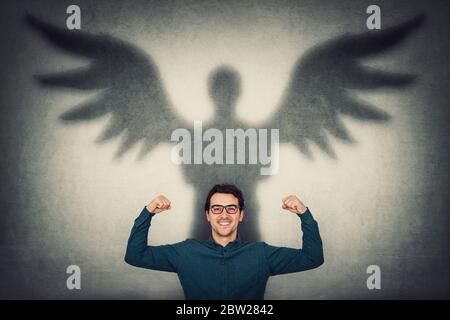 I muscoli flessibili dell'uomo d'affari sicuri immaginano superpotenza. Guy mostra la sua forza, gettando un'ombra supereroe con le ali d'angelo su un muro. Personale