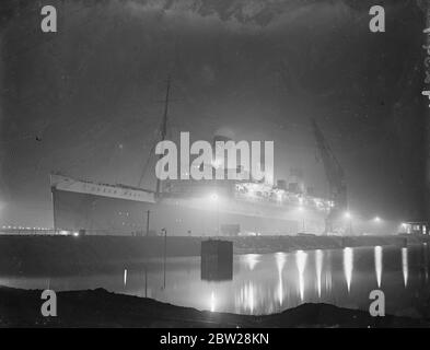 'RMS Queen Mary' nell'abbagliamento dei proiettori. La gigantesca nave 'Queen Mary' è una vista impressionante è il proiettore la illumina nel re George V graving.at Southampton, dove gli uomini lavorano notte e giorno per completare la sua revisione annuale. Spettacoli fotografici, l'alluvione della "Queen Mary" si è illuminata nel molo di incisione di King George V a Southampton. 1 gennaio 1938 Foto Stock