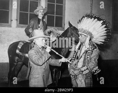 Il 'Wild West' a Parigi !. Club dove tengono vivo il cowboy tradizionale. Uno dei club più pittoreschi di Parigi è il lasso Club, che, pur incontrando al chiuso in una scuola di equitazione, pratica in una capitale europea, l'arte occidentale del 'ropping'. I membri indossano un abito da cowboy. L'ultimo inizia il al club è il sig. Robert Lindneux, il pittore americano, che solennemente fumava un tubo di pace con Oskomon, un capo rosso indiano rinnegato. Foto mostra, MR Robert Lindneux fumo il tubo della pace. Guardato da Oskomon, il capo indiano rosso, e un altro membro del club a cavallo. 25 Novem Foto Stock