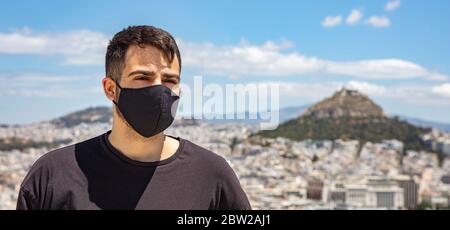 Atene Grecia giorni coronavirus. Giovane uomo che indossa maschera protettiva, paesaggio urbano di Atene con il supporto Lycabettus e sfondo blu cielo. Foto Stock