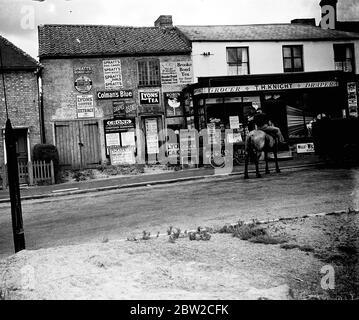 Uomo a cavallo di fronte al negozio di alimentari intorno alla zona di Sevenoaks, Kent. Annunci e segni: T. H. Knight, Draper, Grocer, Cronk di Messer Chartered Surveyors, 138 High Street, Sevenoaks. Brooke Bond Tea, Colman's Blue, Buy Leon's Coffee and Chicory Extract, Leon's Tea, Robin amido per lino, Spratt's Dog Cakes, Otford - Automobile Association, Plaza Super Cinema Poster: Simone Simon - Walter Winchell - Love and Hisses [1937], smalltown, villaggio, rurale, atmosfera, scena di strada. [Box PLANET92157 - numero negativo effettivo 9215 (archivio sconosciuto)] 1937 - 1939, fine 30s, primi 40s ? Foto Stock