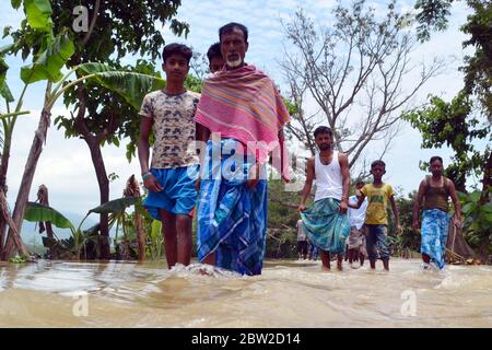 La gente del posto guadi strada sommersa a causa del costante aumento di acqua di inondazione a Kathiatoli, a circa 20 km di distanza da Nagaon in Assam, India Foto Stock