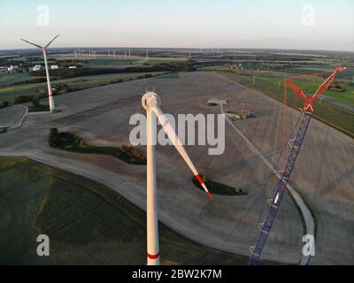 Vista aerea del cantiere di una turbina eolica con gru su pascoli in zona rurale al tramonto. Foto Stock