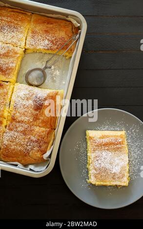 Concetto di cucina greca. Bougatsa greca tradizionale fatta in casa, pasta fillo ripiena di crema su sfondo scuro.Vista dall'alto. Foto Stock