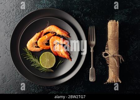 Gamberetti con rosmarino e lime su un piatto nero. Vista dall'alto. Foto Stock